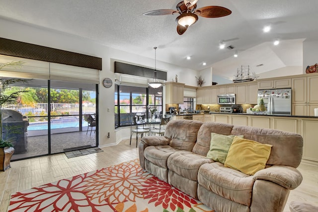 living room with a textured ceiling, ceiling fan, vaulted ceiling, and light wood-type flooring