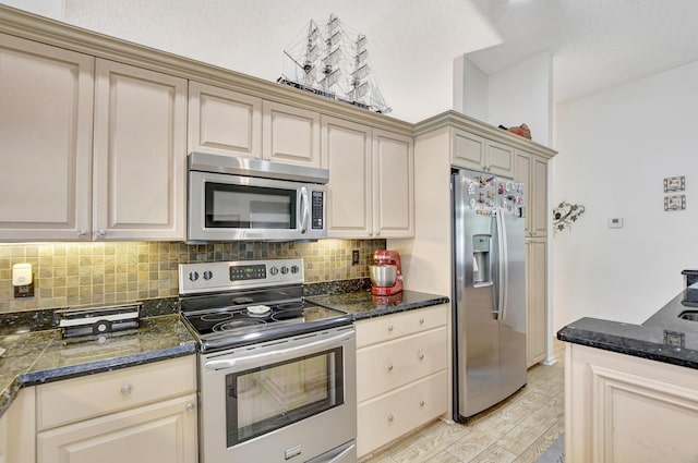 kitchen featuring backsplash, cream cabinets, dark stone countertops, light hardwood / wood-style floors, and stainless steel appliances