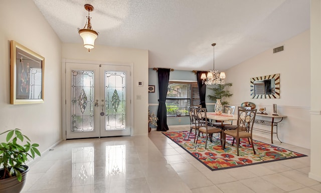 foyer featuring french doors, a textured ceiling, vaulted ceiling, and a notable chandelier