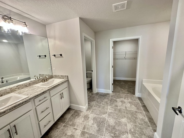 bathroom with a bathing tub, tile patterned flooring, a textured ceiling, toilet, and vanity