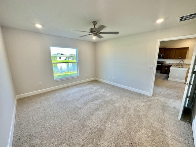 unfurnished room with ceiling fan, sink, and light carpet