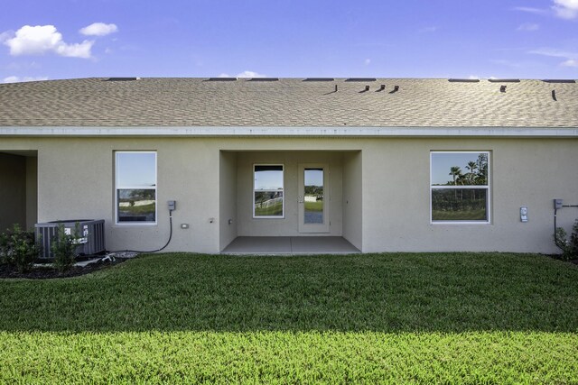 rear view of property featuring central air condition unit, a lawn, and a patio