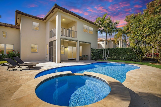 rear view of property with a patio, stucco siding, a pool with connected hot tub, fence, and a balcony