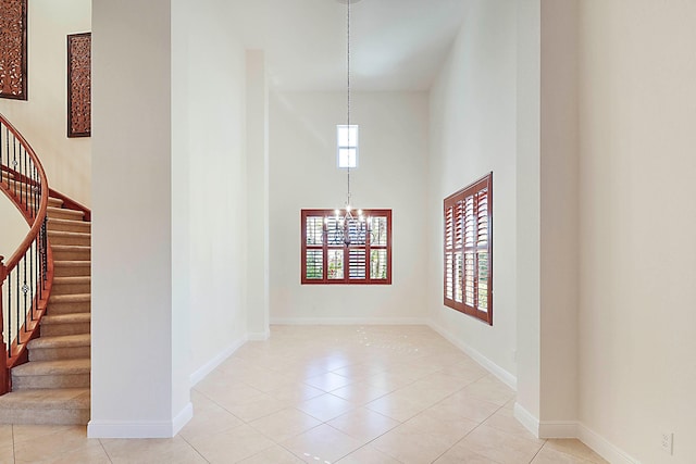 empty room with a notable chandelier, a towering ceiling, stairway, tile patterned flooring, and baseboards