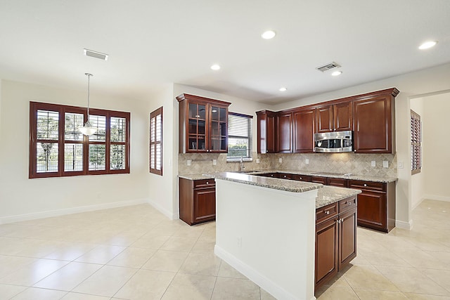 kitchen featuring light stone countertops, a center island, pendant lighting, and backsplash