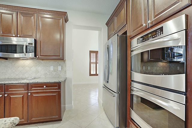 kitchen featuring stainless steel appliances, light stone countertops, light tile patterned floors, and backsplash