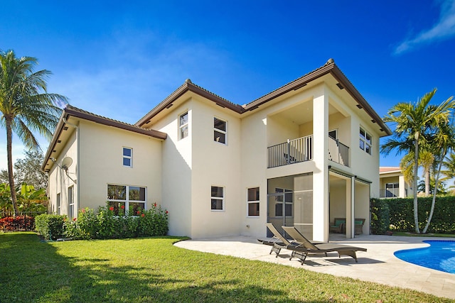 rear view of house featuring a balcony, a fenced in pool, a patio, and a lawn