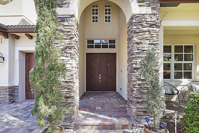 view of exterior entry featuring stone siding and stucco siding