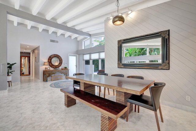 dining area featuring beam ceiling, light tile patterned floors, and wooden walls