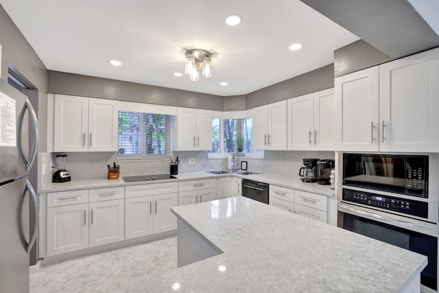 kitchen with sink, tasteful backsplash, light stone counters, white cabinets, and black appliances