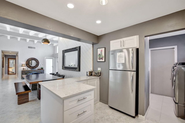 kitchen with washer and clothes dryer, kitchen peninsula, light stone counters, white cabinetry, and stainless steel refrigerator