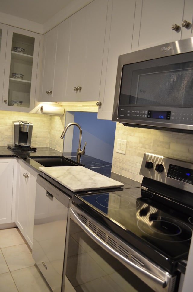 kitchen with decorative backsplash, stainless steel appliances, sink, light tile patterned floors, and white cabinetry