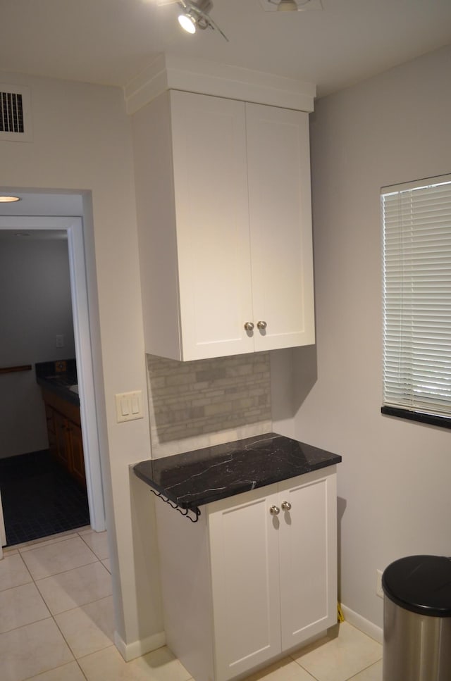 kitchen featuring dark stone countertops, decorative backsplash, white cabinets, and light tile patterned flooring