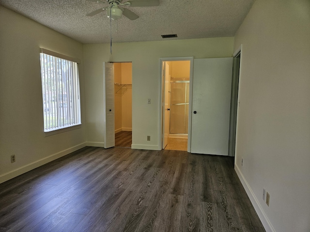 unfurnished bedroom featuring ceiling fan, a textured ceiling, dark hardwood / wood-style flooring, a walk in closet, and a closet