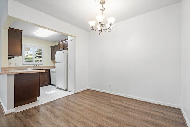 kitchen with light hardwood / wood-style flooring, a chandelier, decorative light fixtures, white appliances, and dark brown cabinets