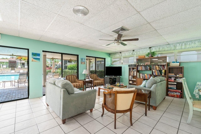 living room with ceiling fan, a drop ceiling, and light tile patterned floors