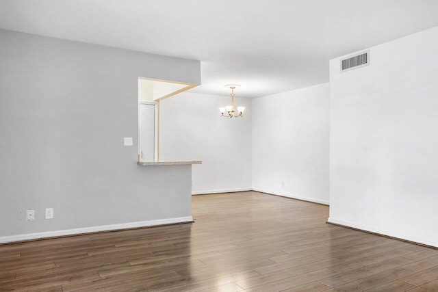 empty room with dark wood-type flooring and an inviting chandelier