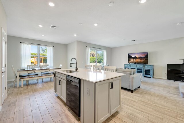 kitchen with an island with sink, sink, dishwasher, and light hardwood / wood-style flooring