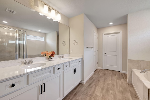 bathroom with dual bowl vanity, hardwood / wood-style flooring, and a bathing tub