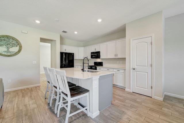 kitchen with black appliances, sink, white cabinets, and a center island with sink