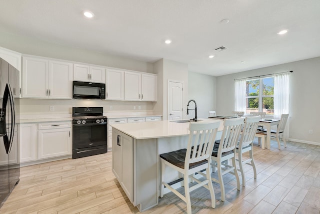 kitchen featuring black appliances, a kitchen island with sink, and white cabinetry