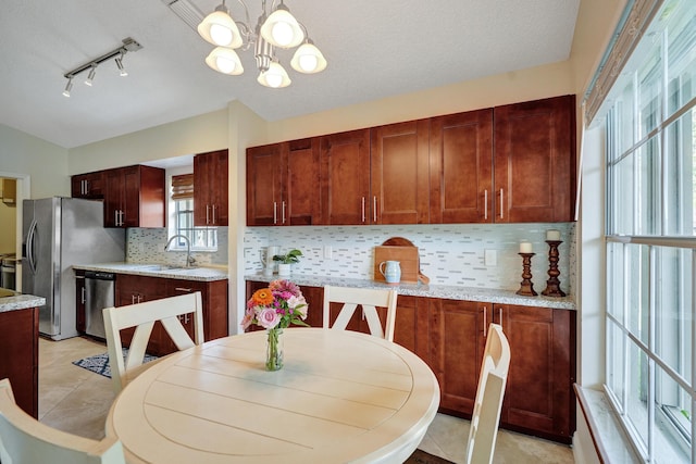 kitchen featuring appliances with stainless steel finishes, light stone counters, hanging light fixtures, a sink, and light tile patterned flooring