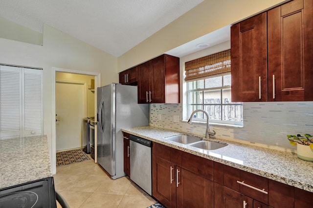 kitchen featuring lofted ceiling, light stone counters, a sink, appliances with stainless steel finishes, and backsplash