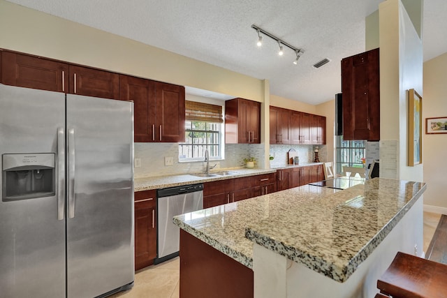 kitchen featuring stainless steel appliances, tasteful backsplash, a sink, and light stone countertops