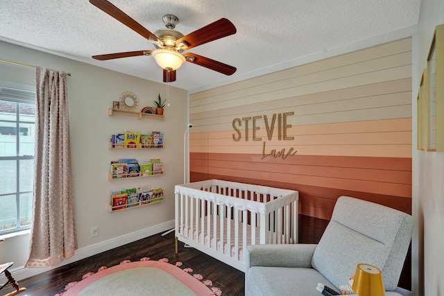 bedroom with a nursery area, wooden walls, dark wood-style flooring, and a textured ceiling