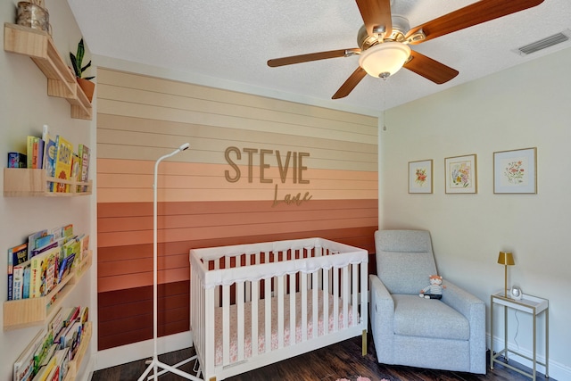 bedroom with wood walls, a textured ceiling, visible vents, and a nursery area