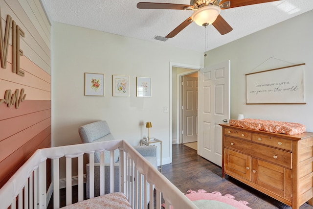 bedroom with dark wood-style flooring, visible vents, wood walls, a textured ceiling, and a nursery area