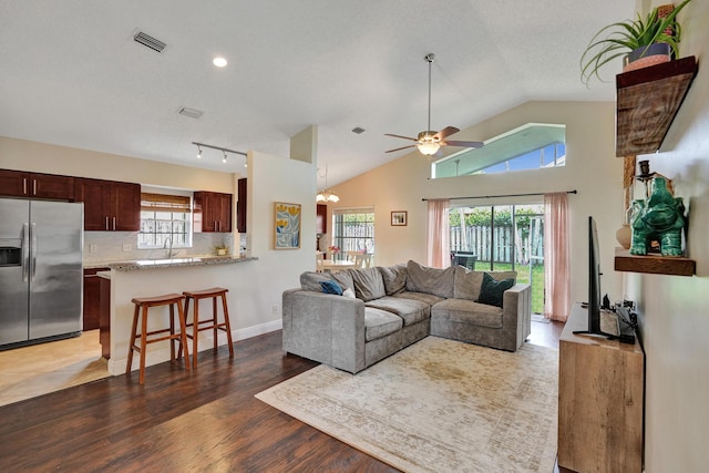 living area featuring vaulted ceiling, dark wood-type flooring, plenty of natural light, and visible vents