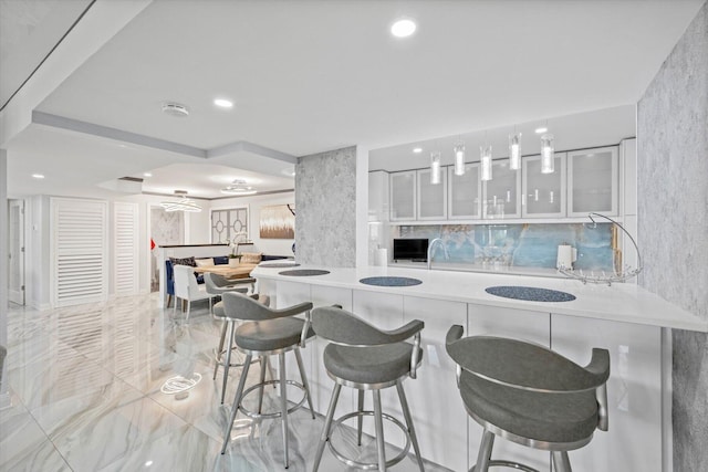 kitchen featuring a breakfast bar, oven, white cabinetry, and hanging light fixtures