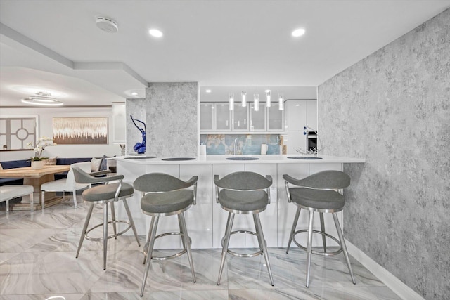 kitchen with a kitchen breakfast bar, decorative backsplash, white cabinetry, and kitchen peninsula