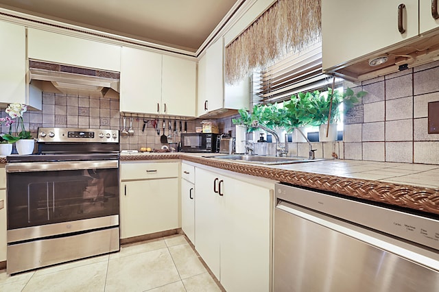 kitchen with custom range hood, appliances with stainless steel finishes, sink, tasteful backsplash, and light tile floors