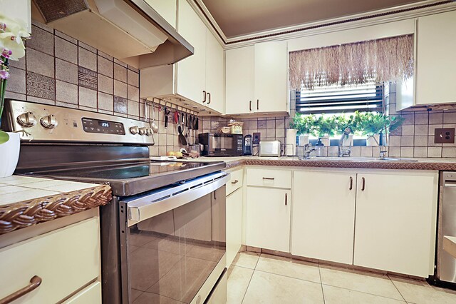 kitchen with stainless steel appliances, custom range hood, backsplash, and light tile floors