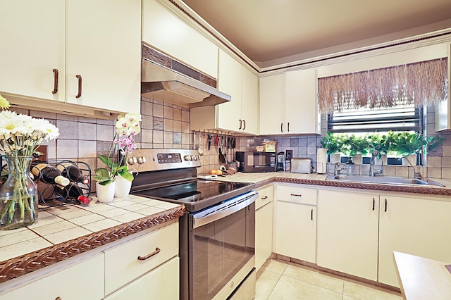 kitchen with stainless steel range with electric cooktop, premium range hood, sink, tasteful backsplash, and light tile floors