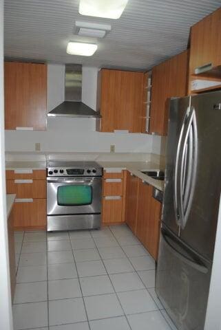 kitchen featuring light tile patterned floors, stainless steel appliances, and wall chimney exhaust hood