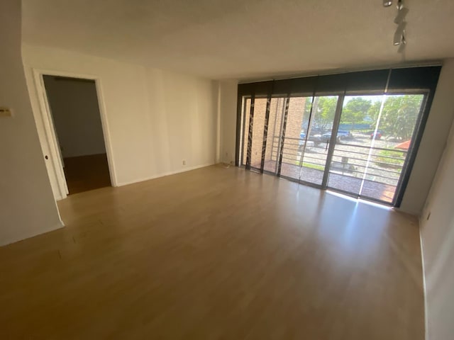 empty room featuring track lighting, hardwood / wood-style floors, and expansive windows