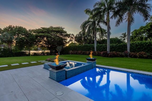 pool at dusk with a lawn, an in ground hot tub, and a patio