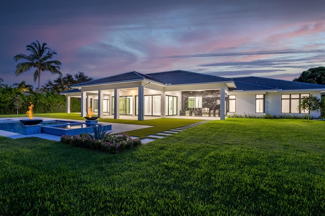 back house at dusk featuring a patio, a pool with hot tub, and a lawn