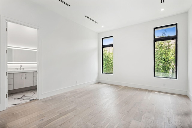 unfurnished bedroom featuring light wood-type flooring, multiple windows, and connected bathroom