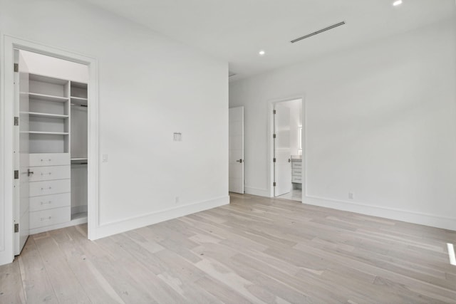 unfurnished bedroom with a walk in closet, ensuite bathroom, and light hardwood / wood-style flooring