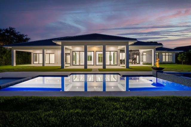 back house at dusk featuring a lawn and a patio area