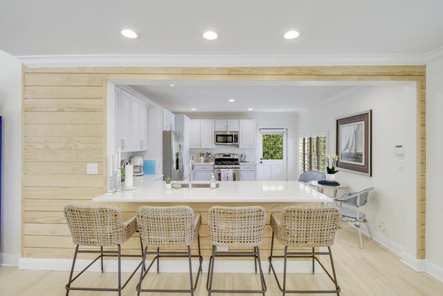 kitchen featuring white cabinetry, light hardwood / wood-style flooring, stainless steel appliances, kitchen peninsula, and a breakfast bar