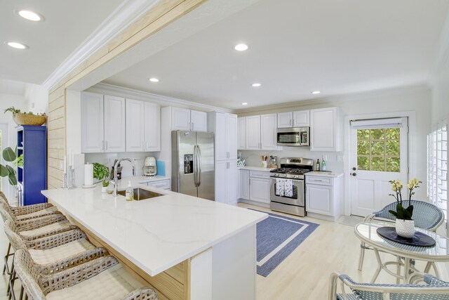 kitchen with light hardwood / wood-style flooring, kitchen peninsula, stainless steel appliances, a kitchen breakfast bar, and sink