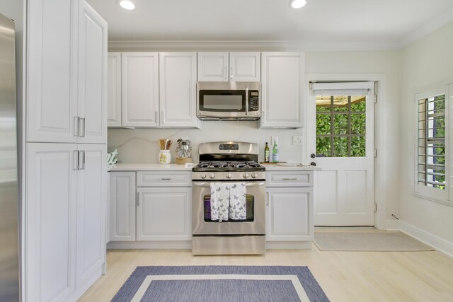 kitchen with stainless steel appliances, white cabinetry, ornamental molding, and light hardwood / wood-style flooring