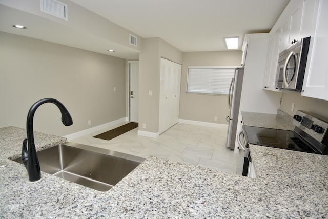 kitchen with white cabinets, stainless steel appliances, light stone countertops, and sink