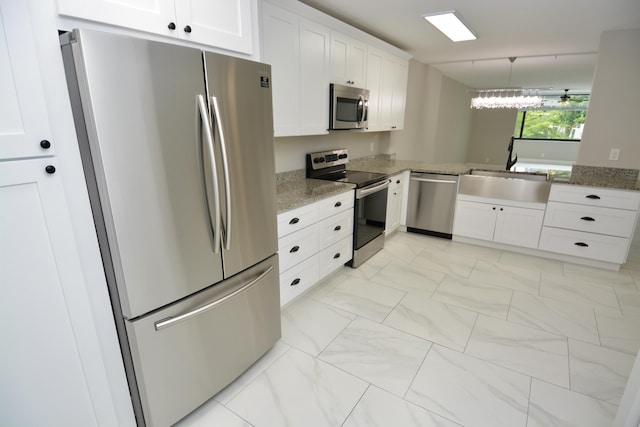 kitchen with appliances with stainless steel finishes, sink, stone counters, white cabinets, and hanging light fixtures