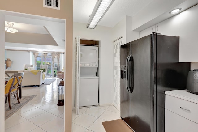 kitchen featuring white cabinets, black fridge, stacked washer / dryer, and light tile patterned flooring